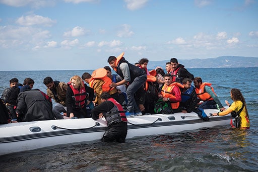 A volunteer lifeguard assists migrants out of their boat after they landed on the Greek island of Lesbos, near the town of Skala Sikamineas. The coastline of Turkey is visible on the right side of the photo. Joel Carillet image.